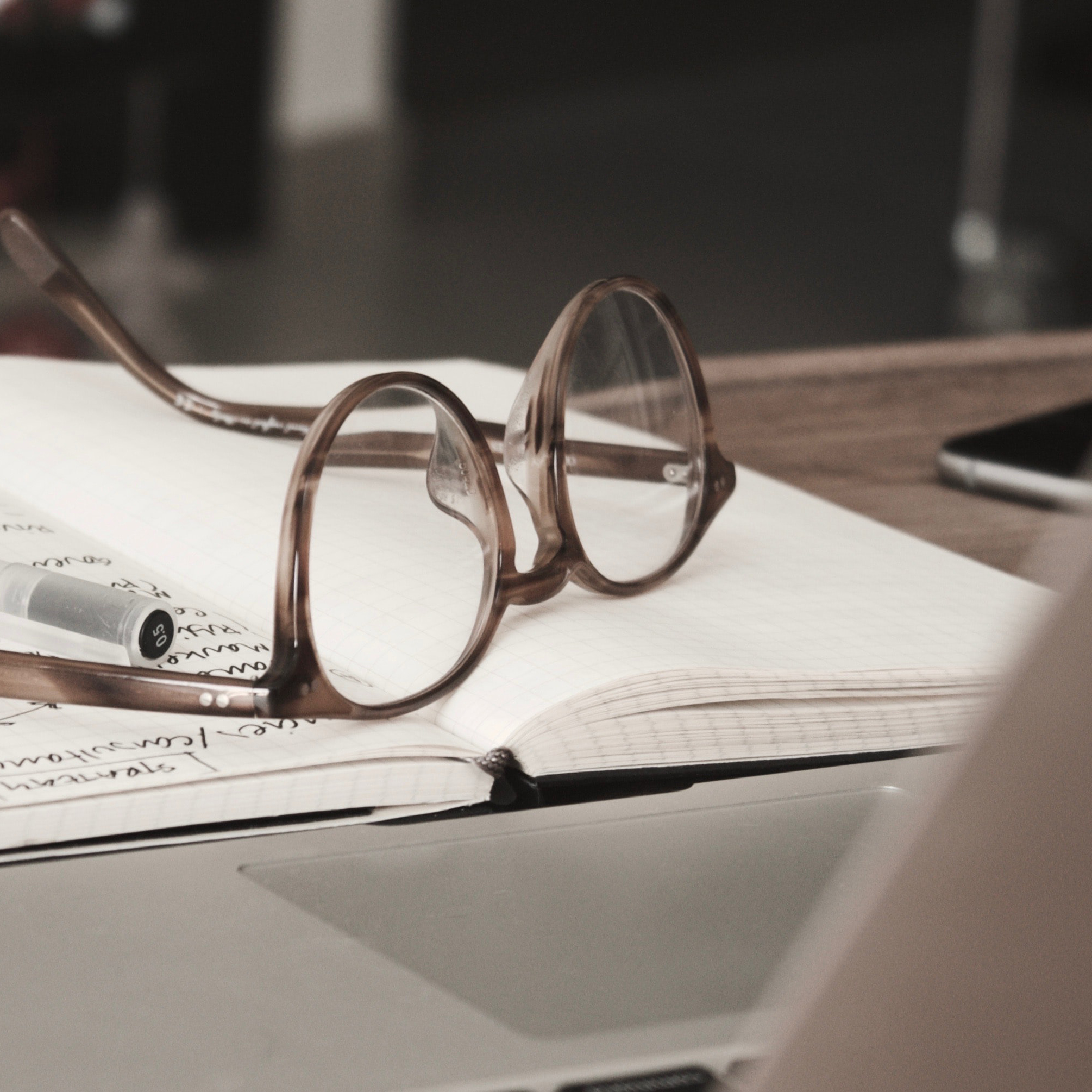 Glasses sitting on a journal opened up on a table near a laptop