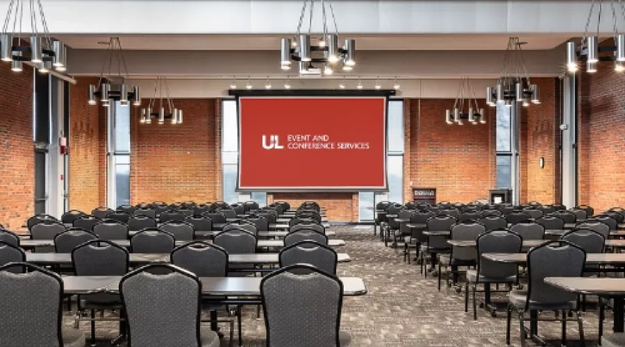 Ballroom with projector screen and multiple rows of tables and chairs