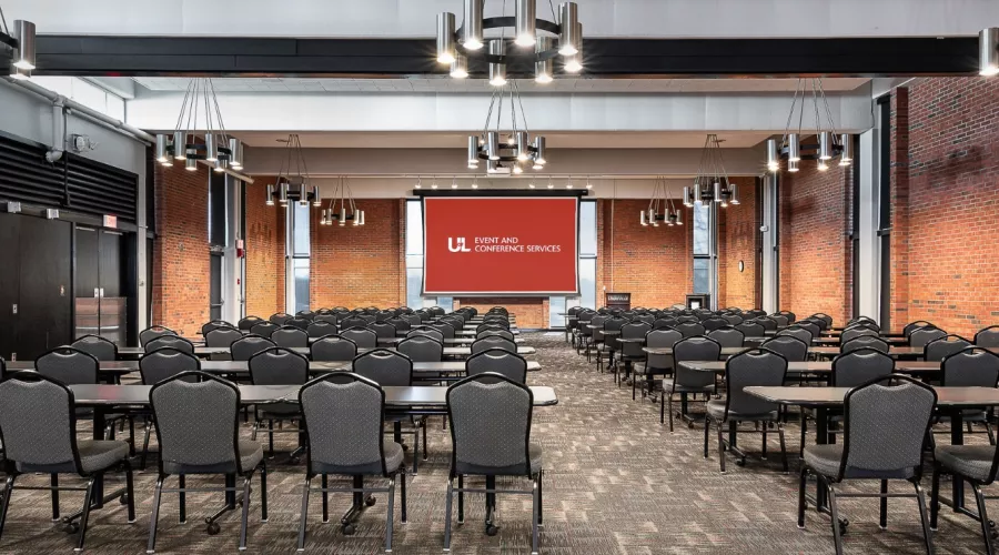 Balltoom with projector screen and multiple rows of tables and chairs
