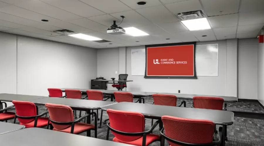 Classroom with projector screen and multiple rows of tables and chairs