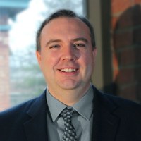A man wearing formal clothing standing in front of a brick wall. 