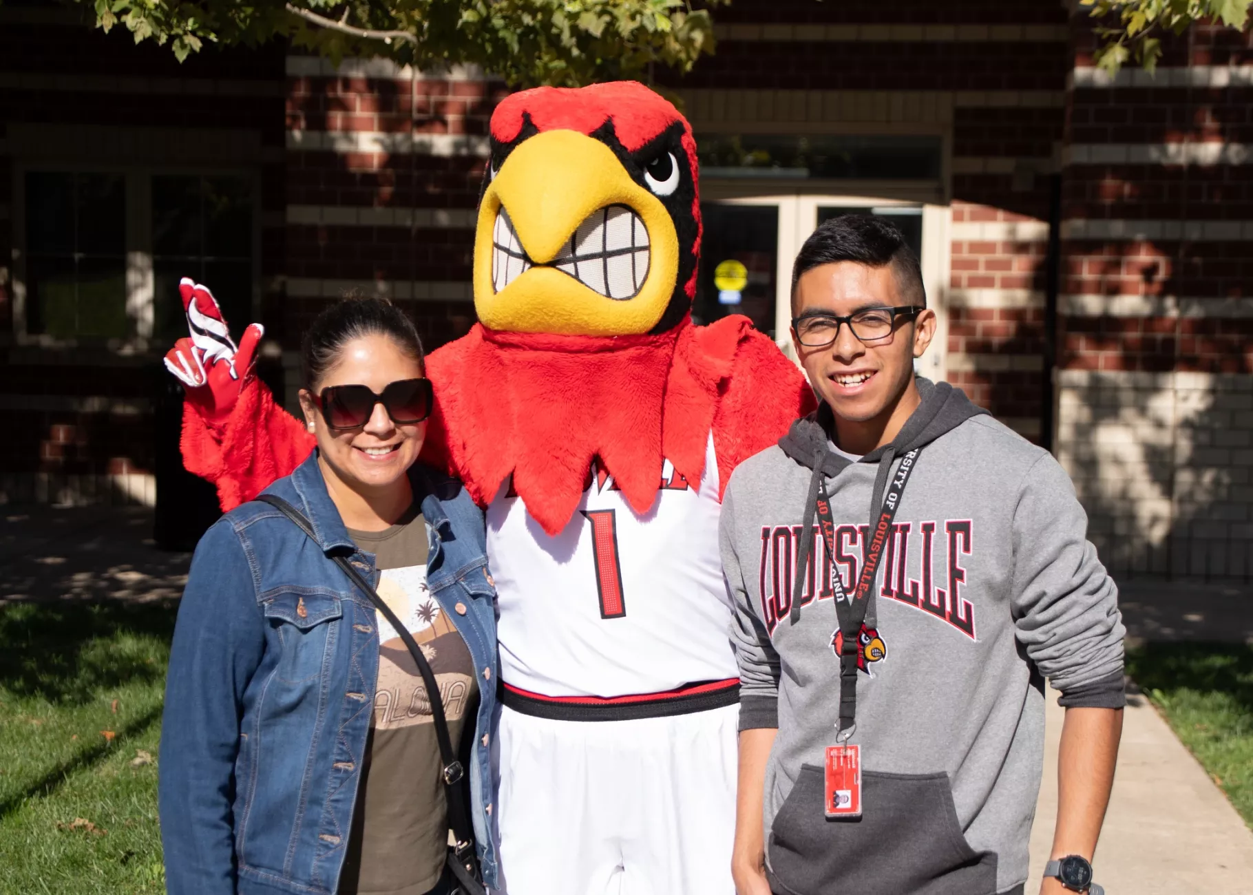 A parent and student posing with Louie, the cardinal mascot, on move-in day at Community Park.