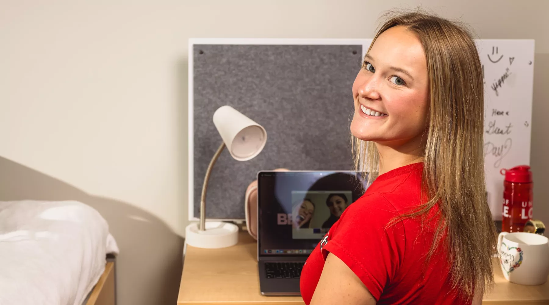 A student sits at a desk in a dorm room on campus