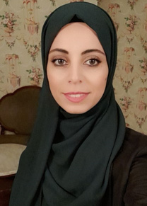 A smiling woman in a black hijab sits in front of flowered wallpaper