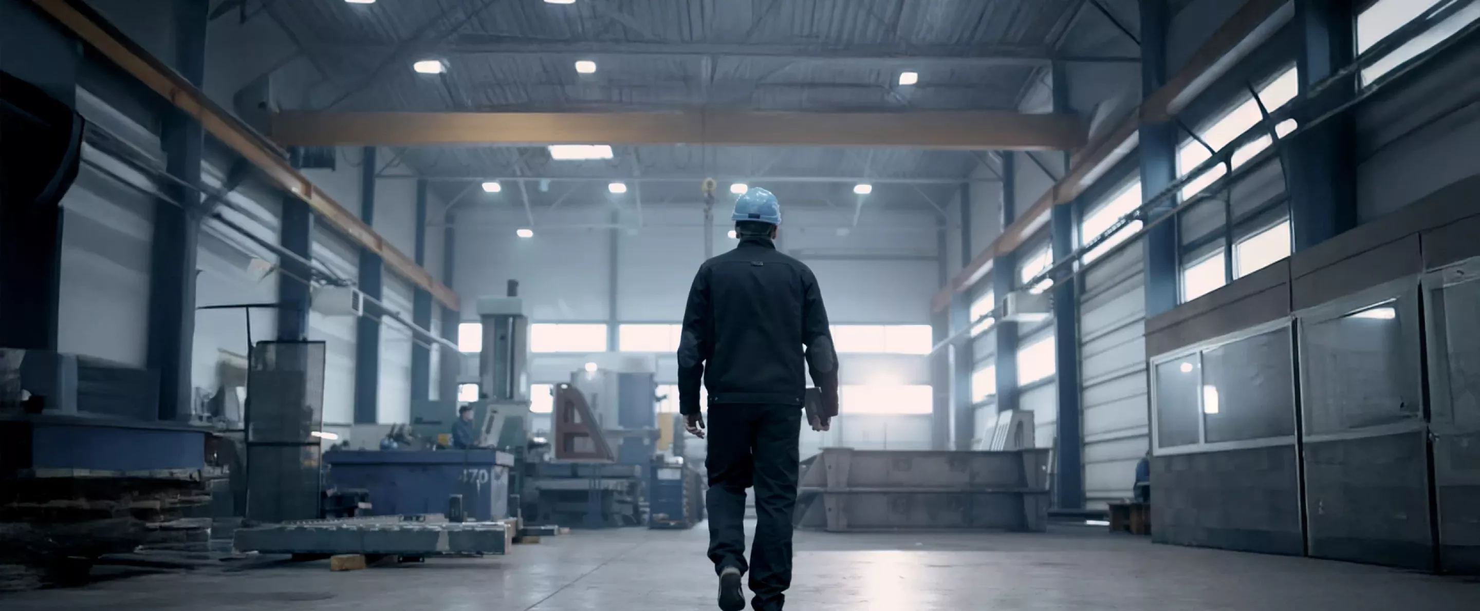 Person in an industrial setting with a hard hat walking away from the camera.