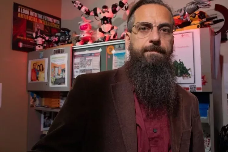 Roman Yampolskiy posing in his office, which is filled with toy robots and posters related to AI.